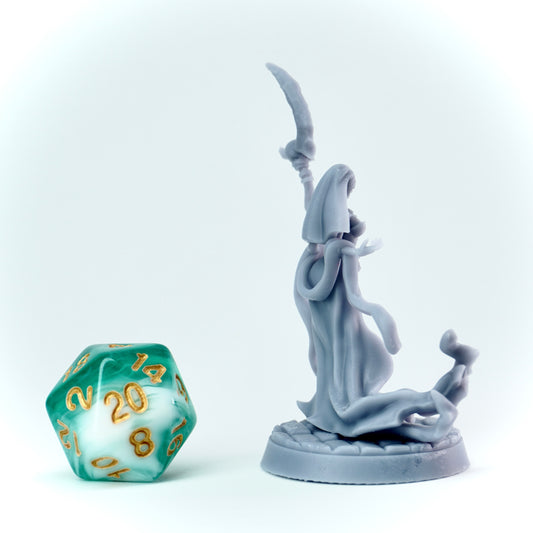 Gray figurine of a evil nun in a hooded robe holding a scythe next to a green polyhedral dice on a white background