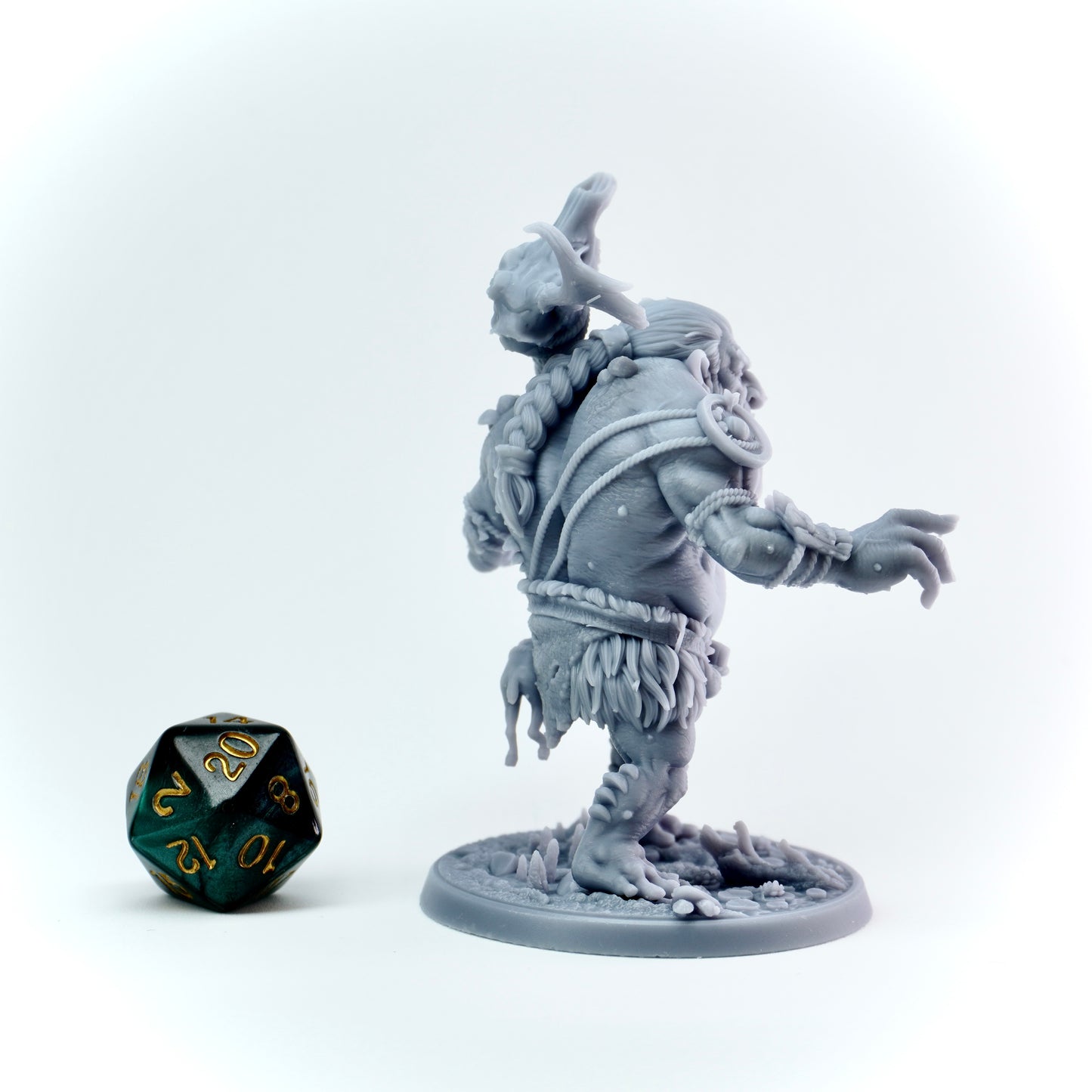 Gray miniature figure of a troll warrior with a green and black polyhedral dice on a white background