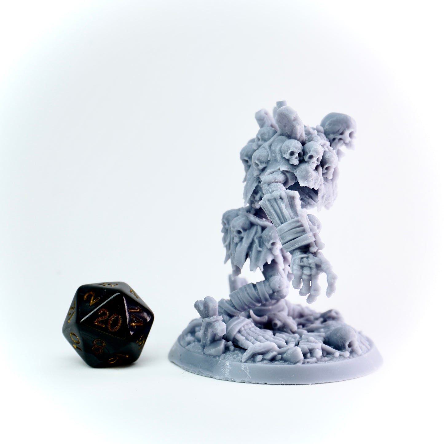 Gray miniature figurine with intricate details on a white background, next to a black and gold die.