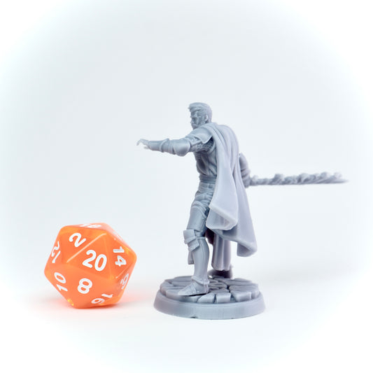 Gray miniature figure of a warrior with a cape next to an orange polyhedral dice on a white background