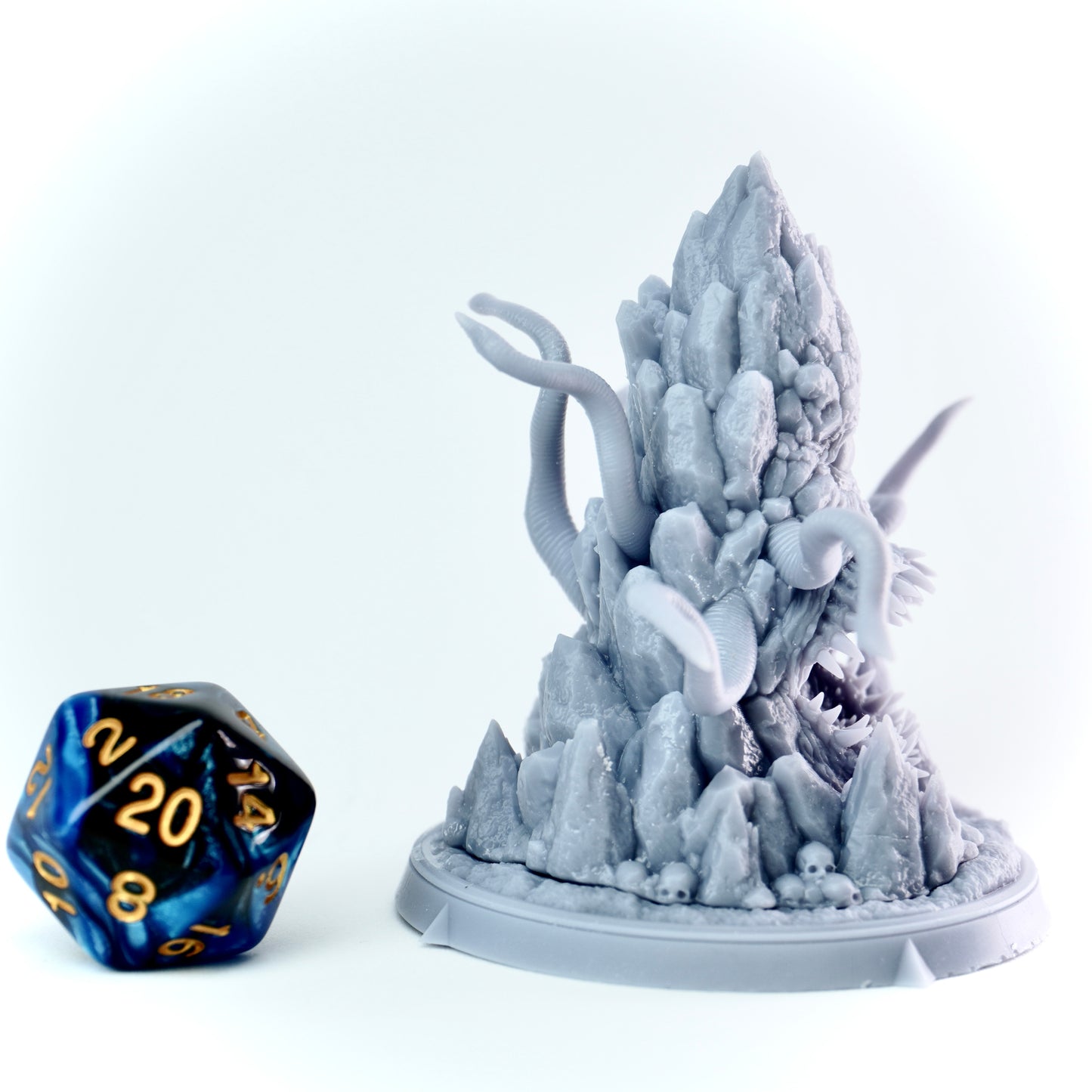 Gray fantasy figurine with a mimic-like creature on a white background, next to a blue and black die.