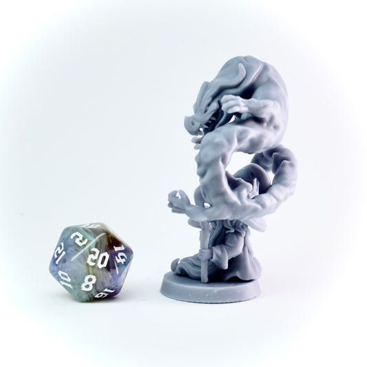 Gray fantasy figurine with a staff next to a polyhedral dice on a white background