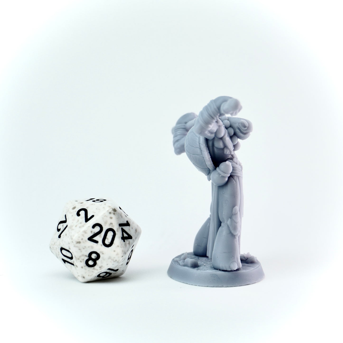 Gray miniature figure with a staff next to a twenty-sided die on a white background