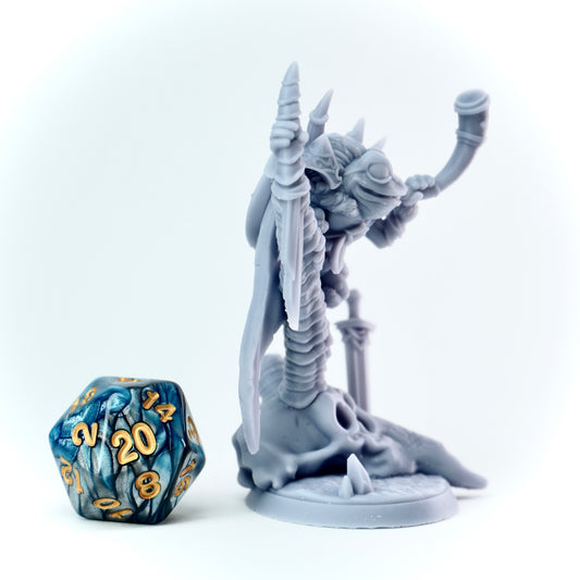 Gray fantasy frog figurine with a blue and gold polyhedral dice on a white background