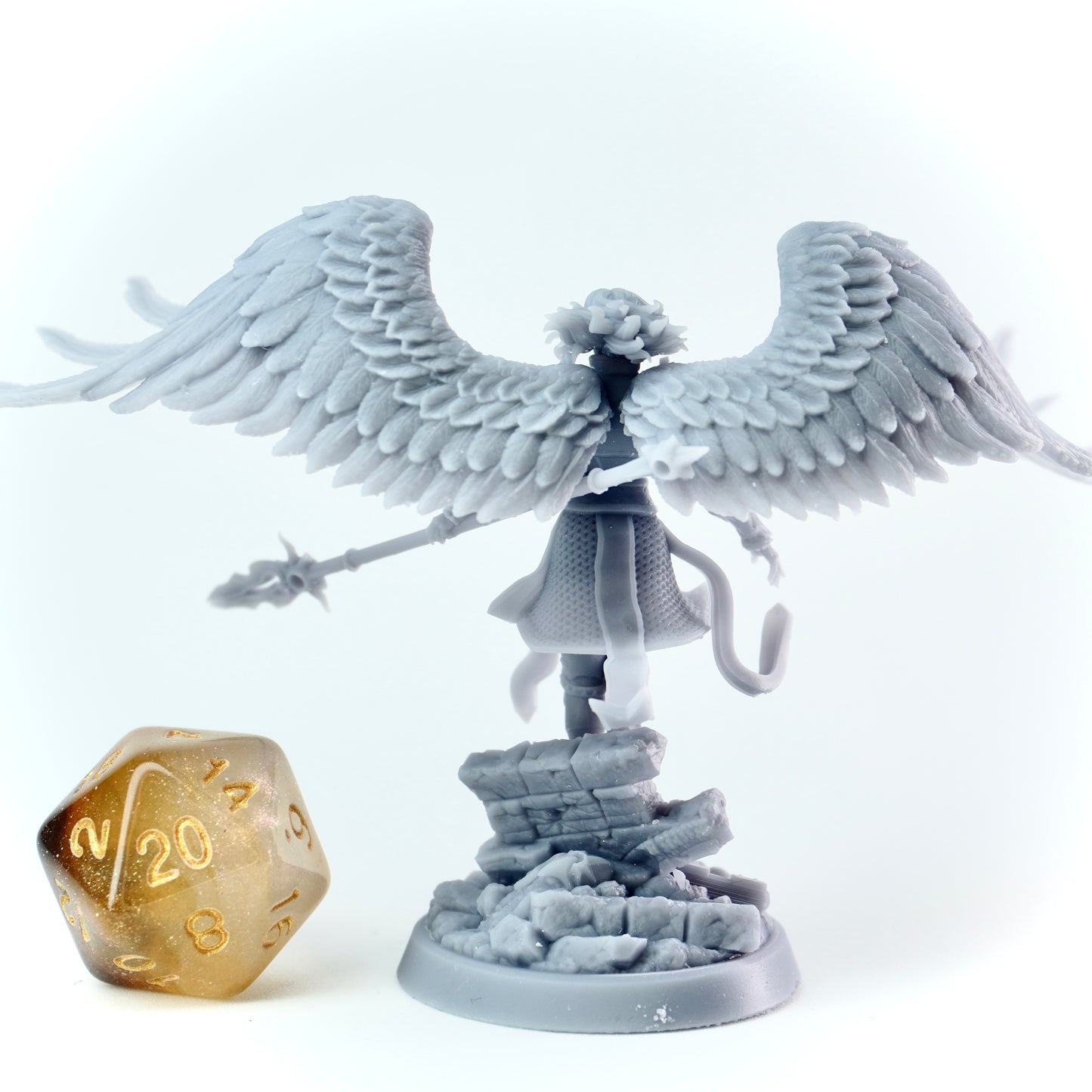 Gray angel figurine with wings and a spear, next to a gold polyhedral dice on a white background