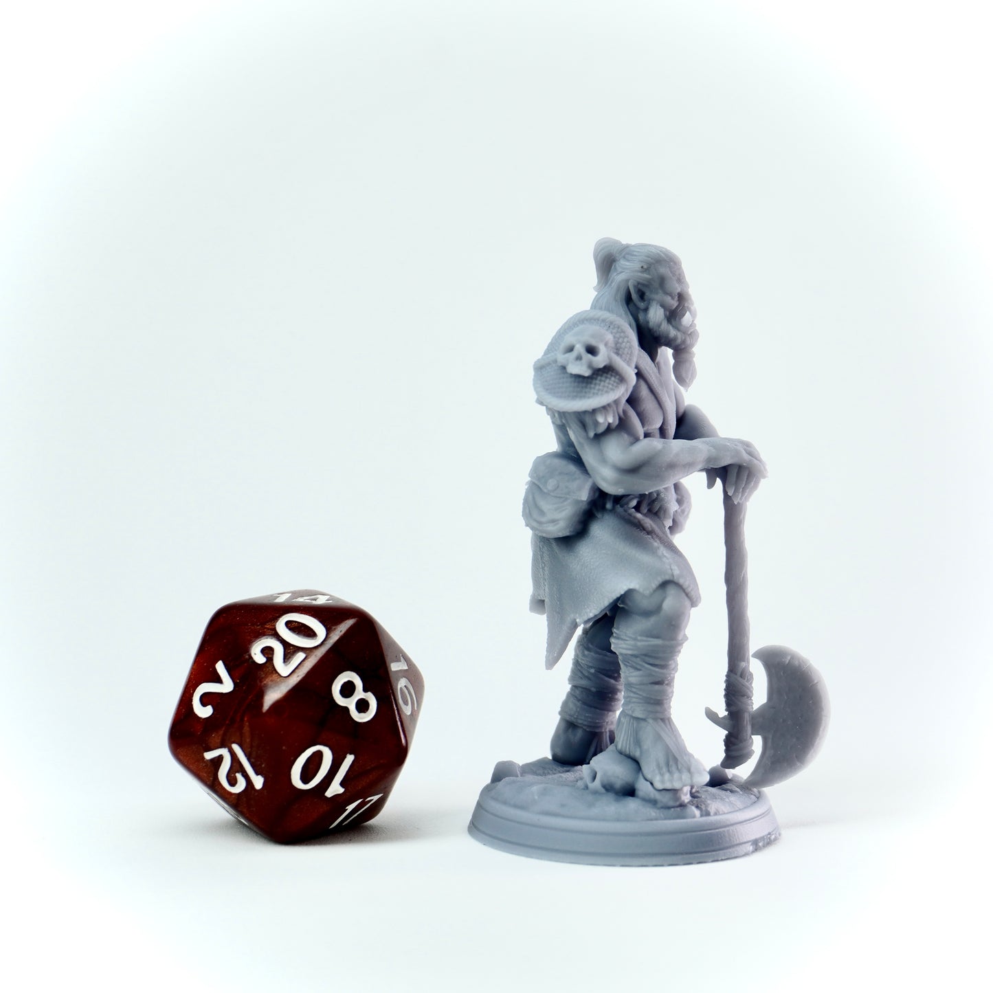 Gray miniature figure of a orc warrior with an axe next to a 20-sided die on a white background