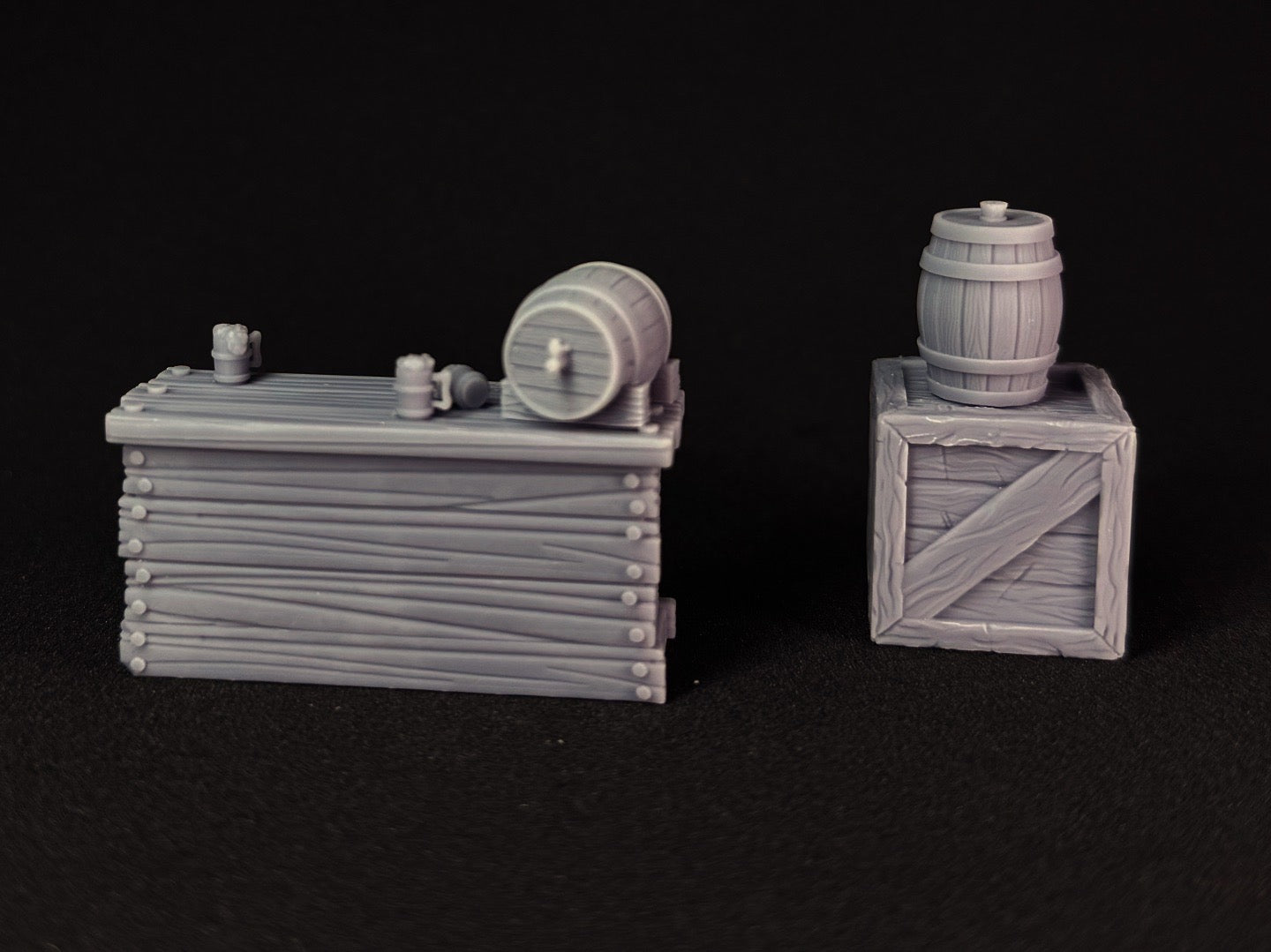 Two miniature wooden crates with barrels on top with a black background