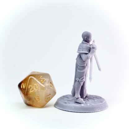 Gray miniature figure of a warrior with a sword next to a gold polyhedral dice on a white background