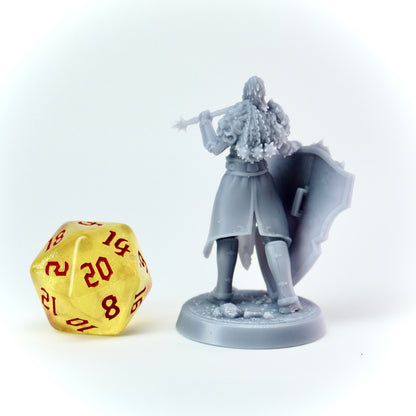 Gray fantasy figurine with a shield and a mace next to a yellow polyhedral dice on a white background