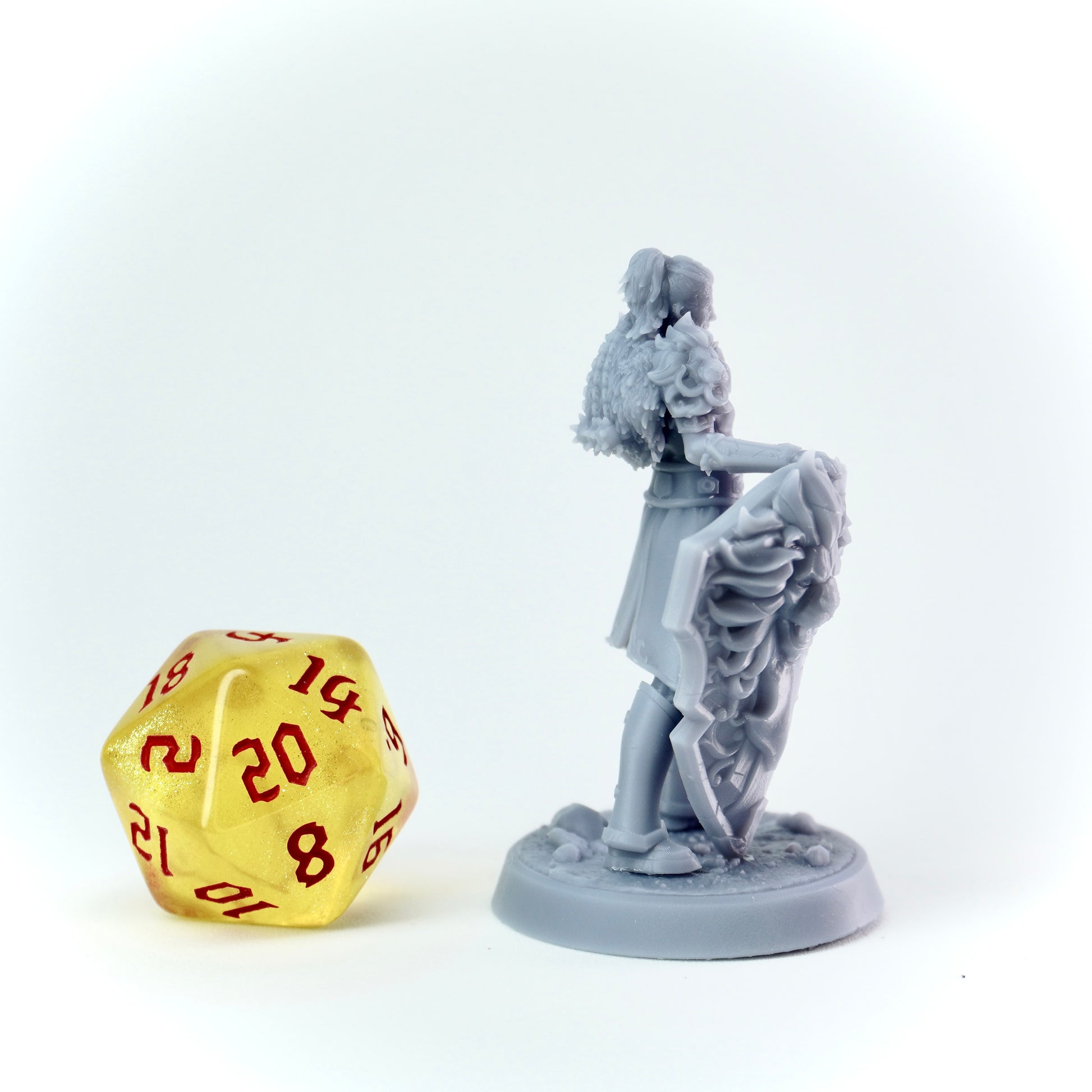 Gray figurine of a person with a shield next to a gold D20 dice on a white background