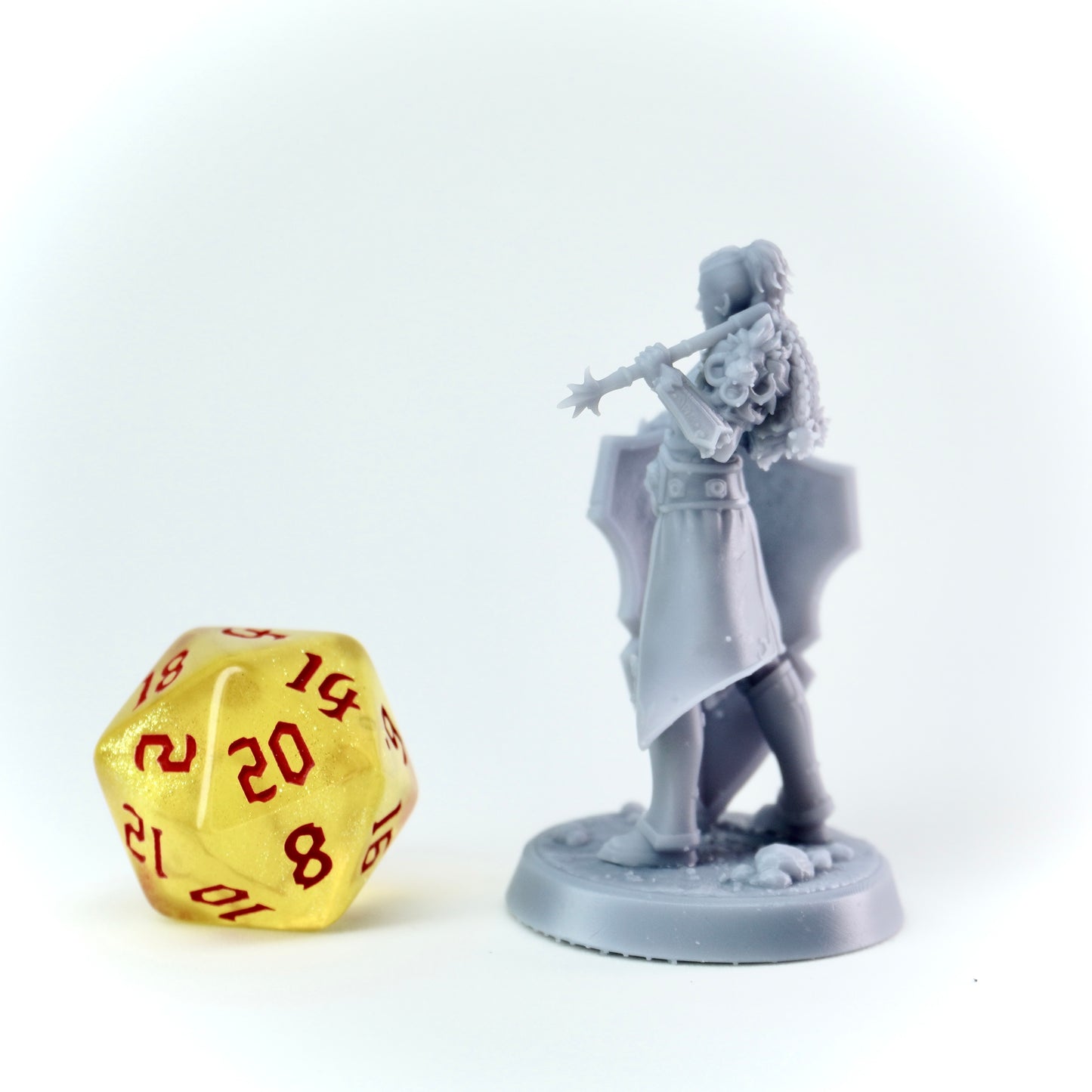 Gray miniature figure of a warrior with a mace next to a gold die with red numbers on a white background