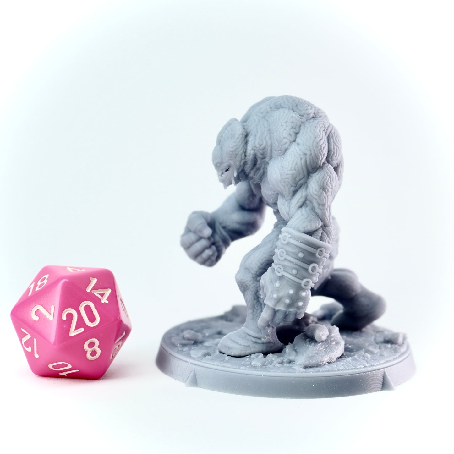 Gray miniature figure of a creature on a white base with a pink twenty-sided die next to it.