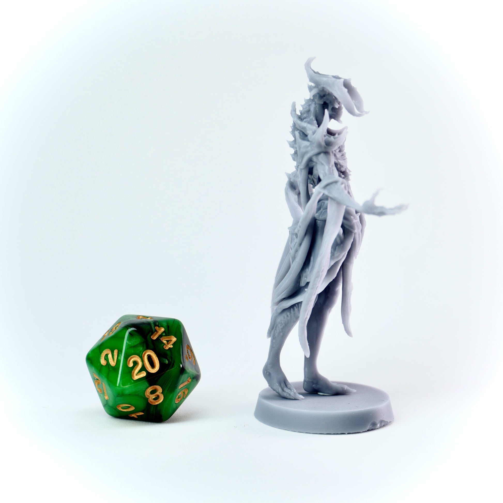Gray fantasy figurine next to a green polyhedral dice on a white background