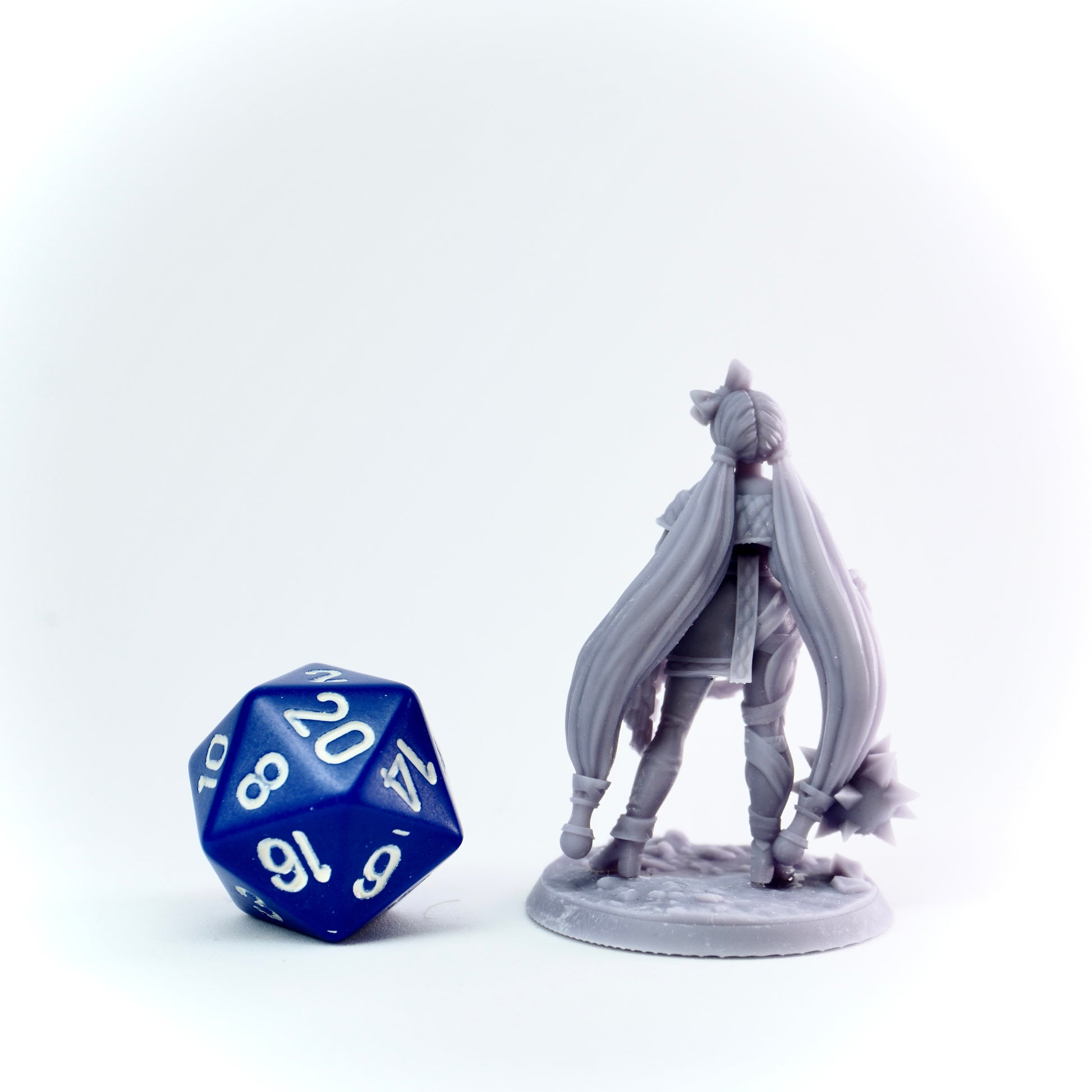 Gray fantasy figurine with long hair next to a blue polyhedral dice on a white background