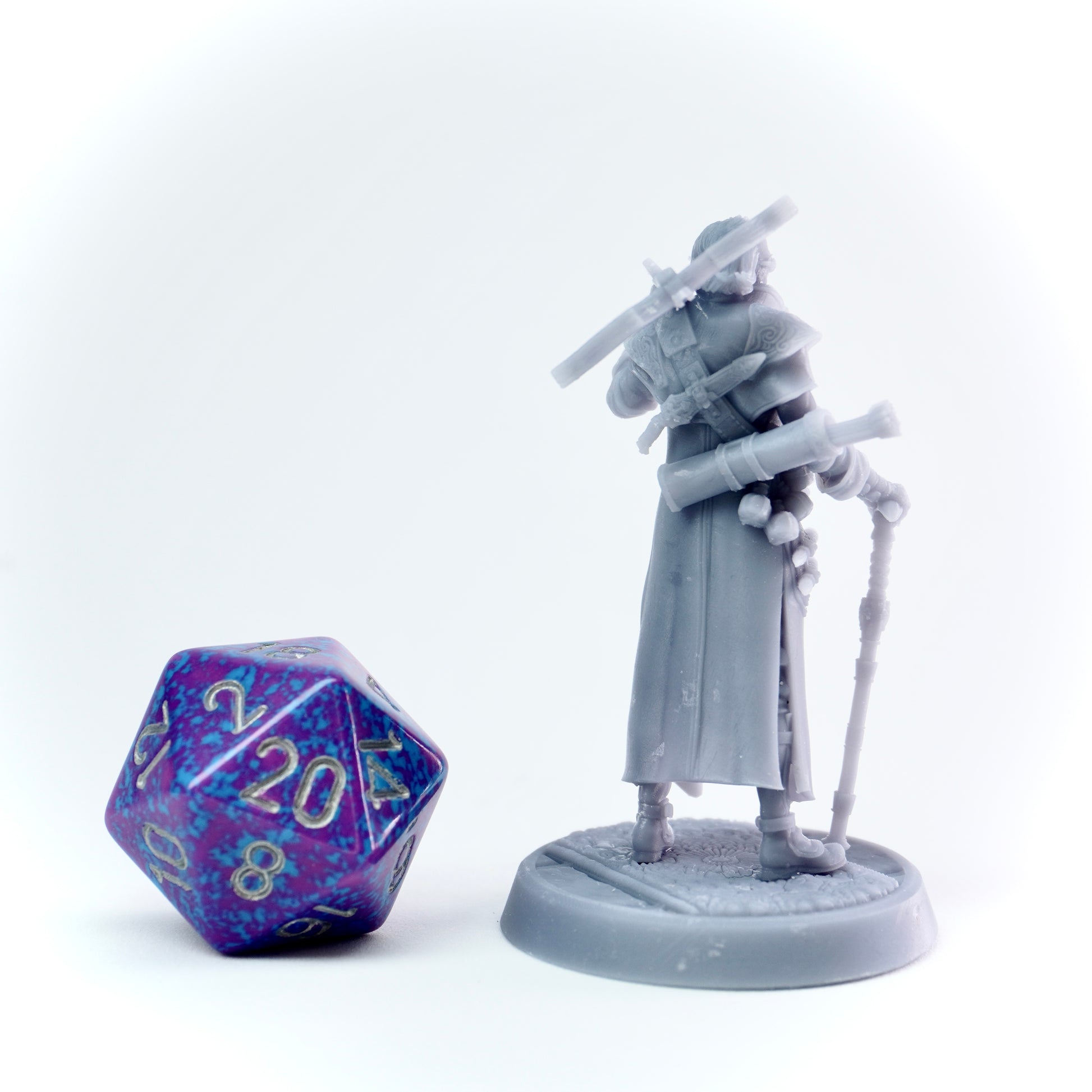 Gray figurine of a cloaked character with a cane next to a purple polyhedral dice on a white background