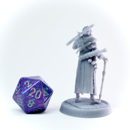 Gray figurine of a cloaked character with a cane next to a purple polyhedral dice on a white background