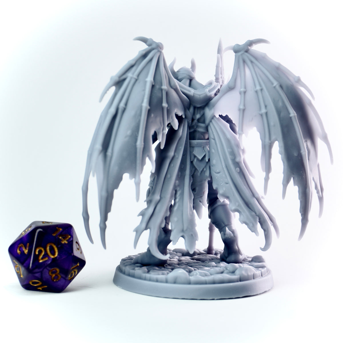 Fantasy zombie figurine with wings next to a polyhedral dice on a white background
