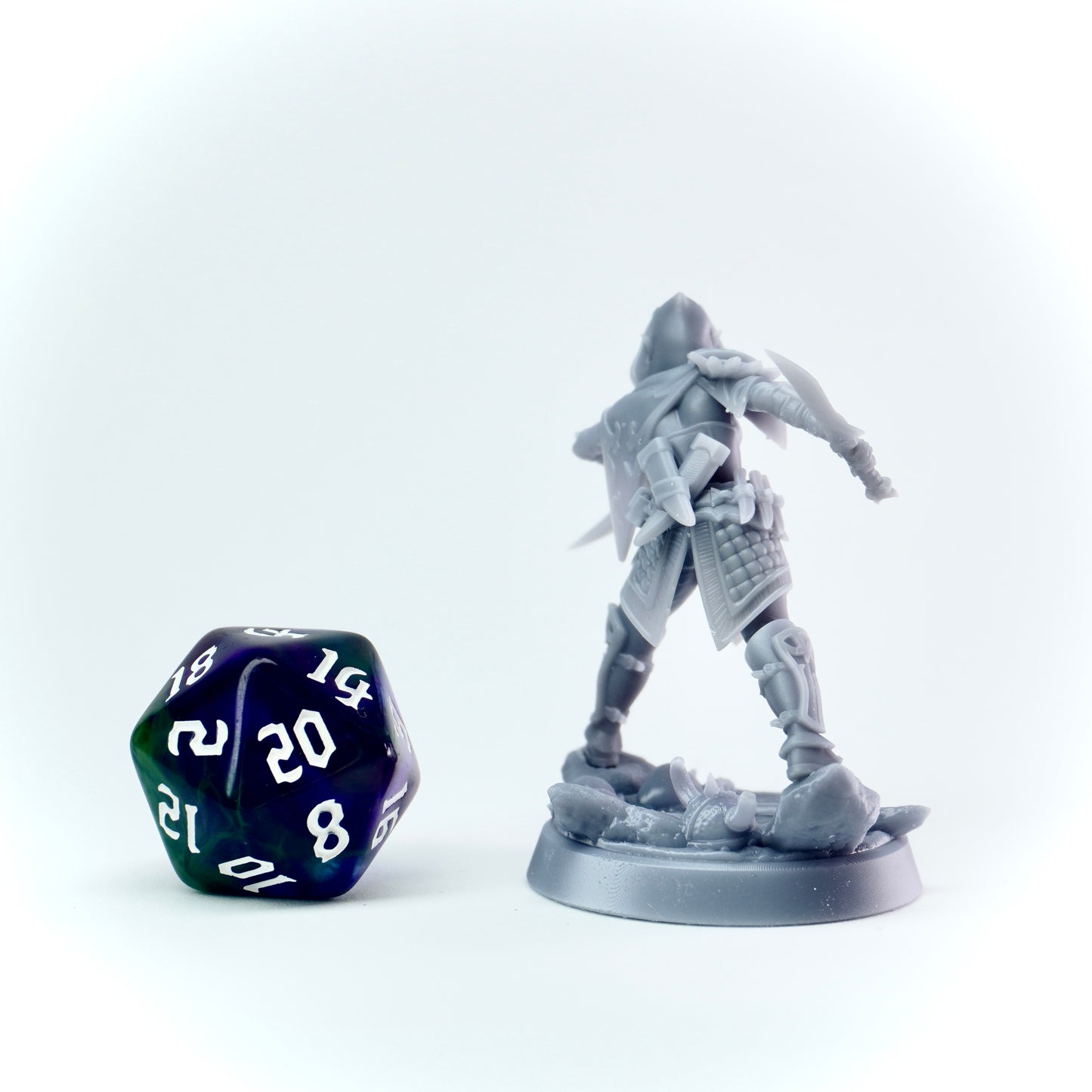 Gray fantasy rogue figurine next to a polyhedral dice on a white background