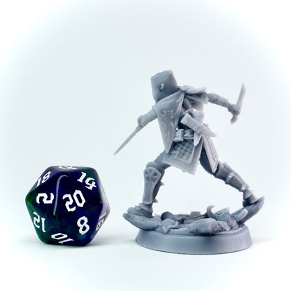 Gray miniature figure of a rogue with a daggers, standing on a base, next to a 20-sided die on a white background.