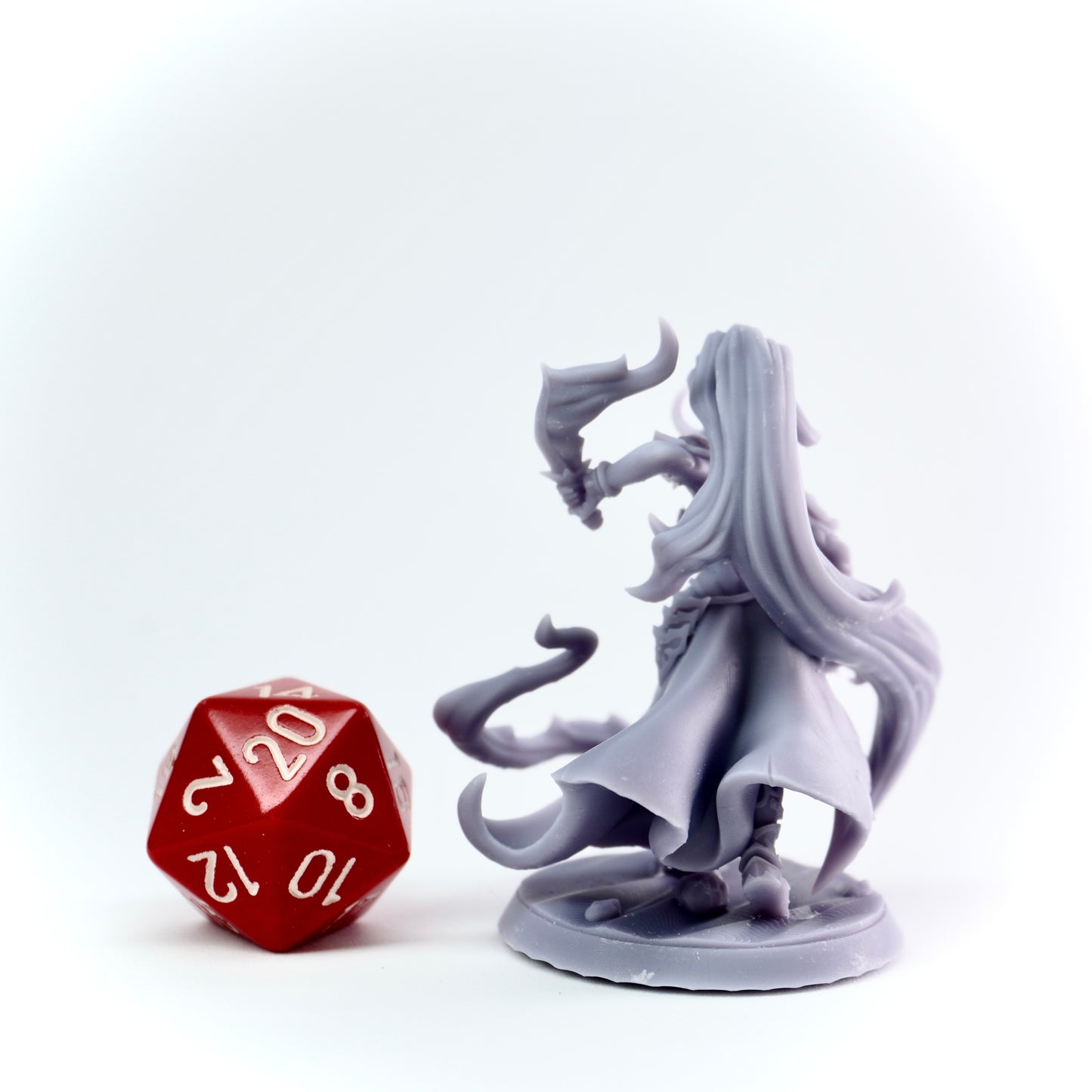 Gray fantasy figurine next to a red polyhedral dice on a white background