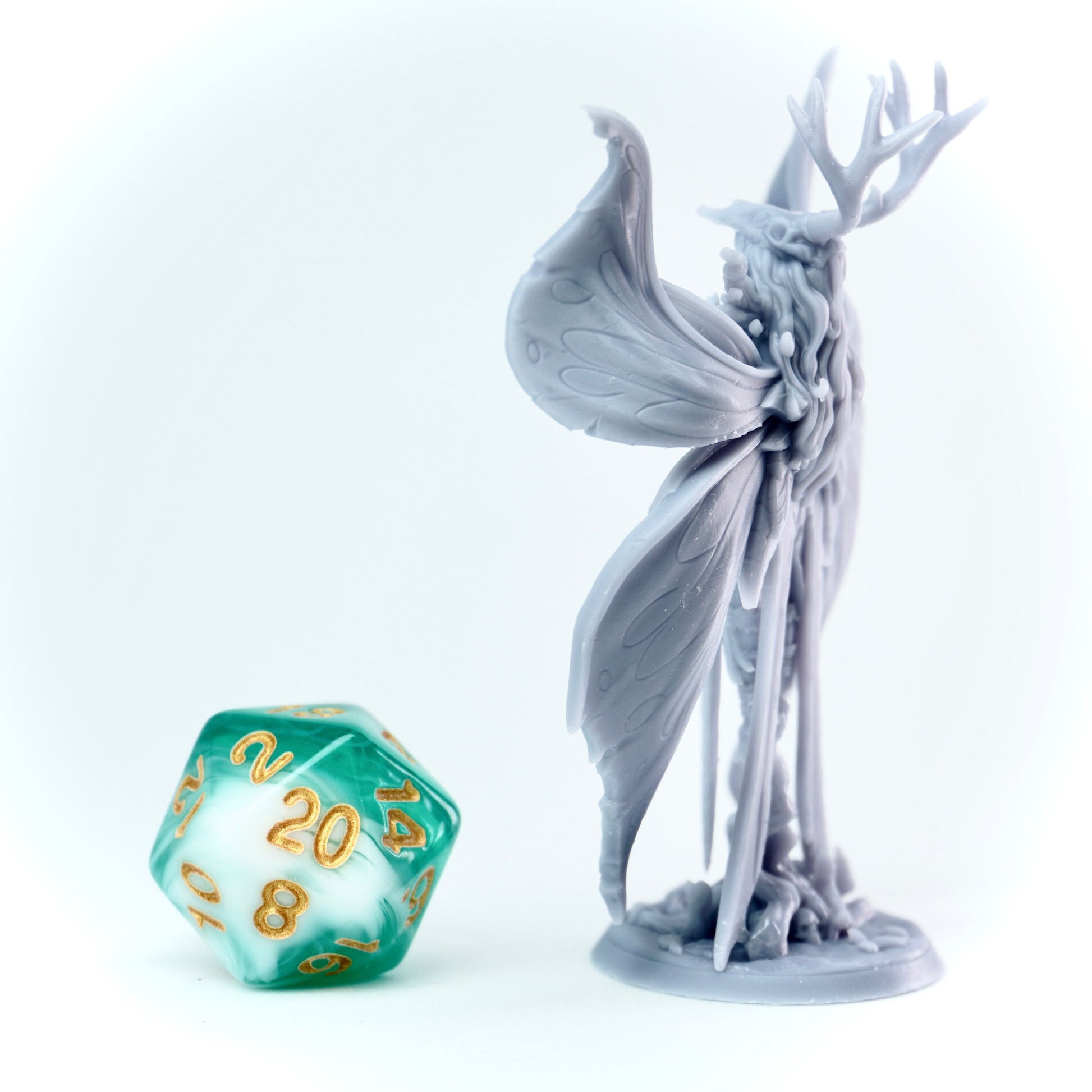 Gray fantasy fey-like figurine with antlers next to a green polyhedral dice on a white background