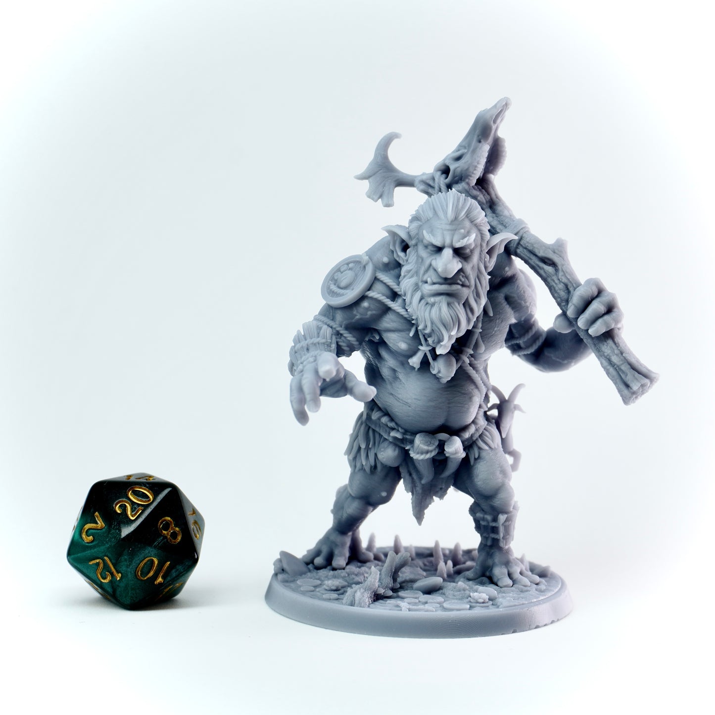 Gray fantasy figurine with a weapon next to a green polyhedral dice on a white background