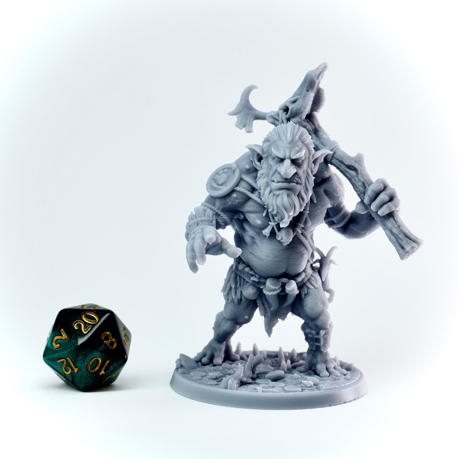 Gray fantasy figurine with a weapon next to a green polyhedral dice on a white background