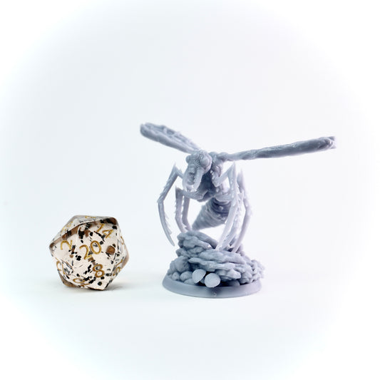Grey miniature figure of a spider-like creature with a large die on a white background