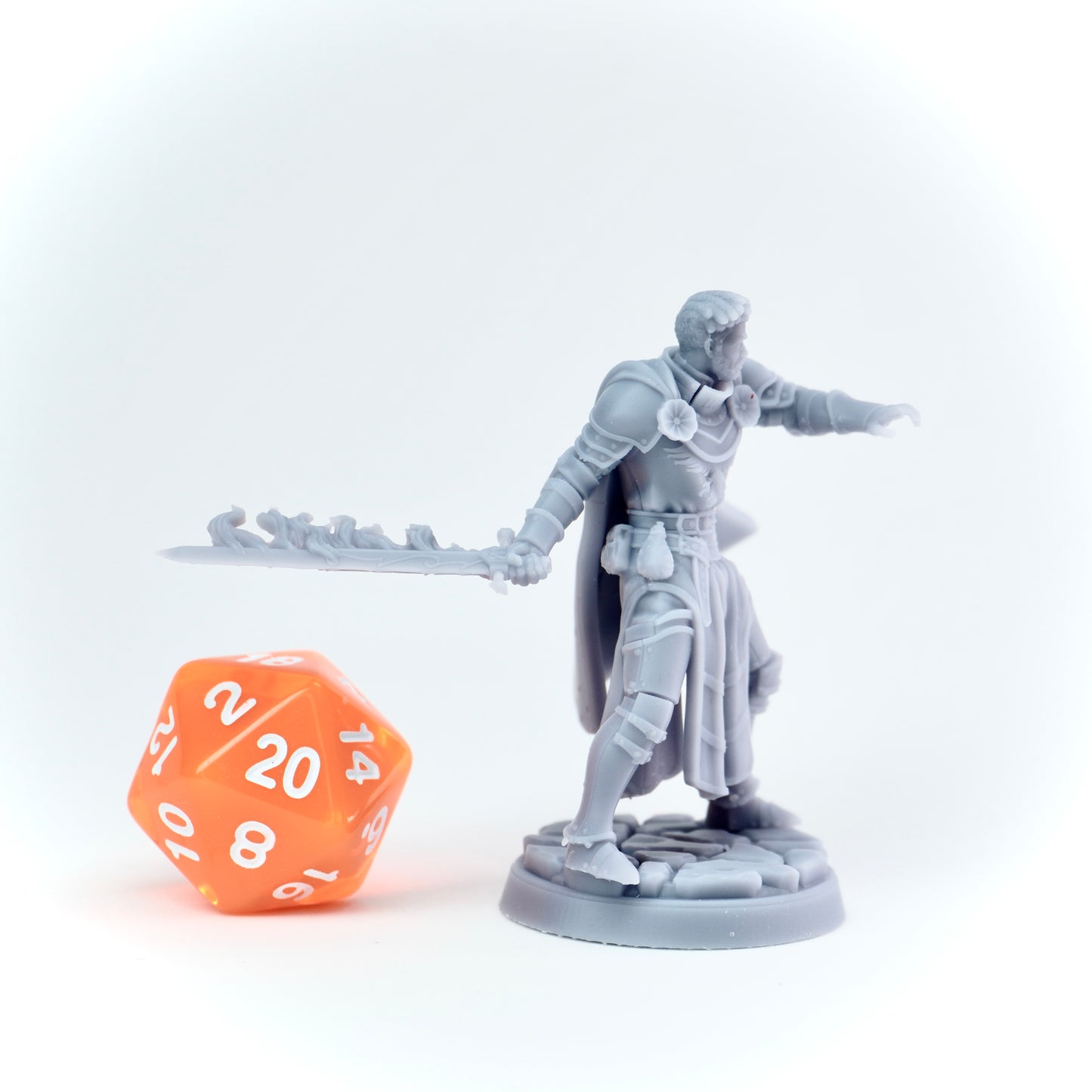Gray fantasy figurine with a sword next to an orange polyhedral dice on a white background