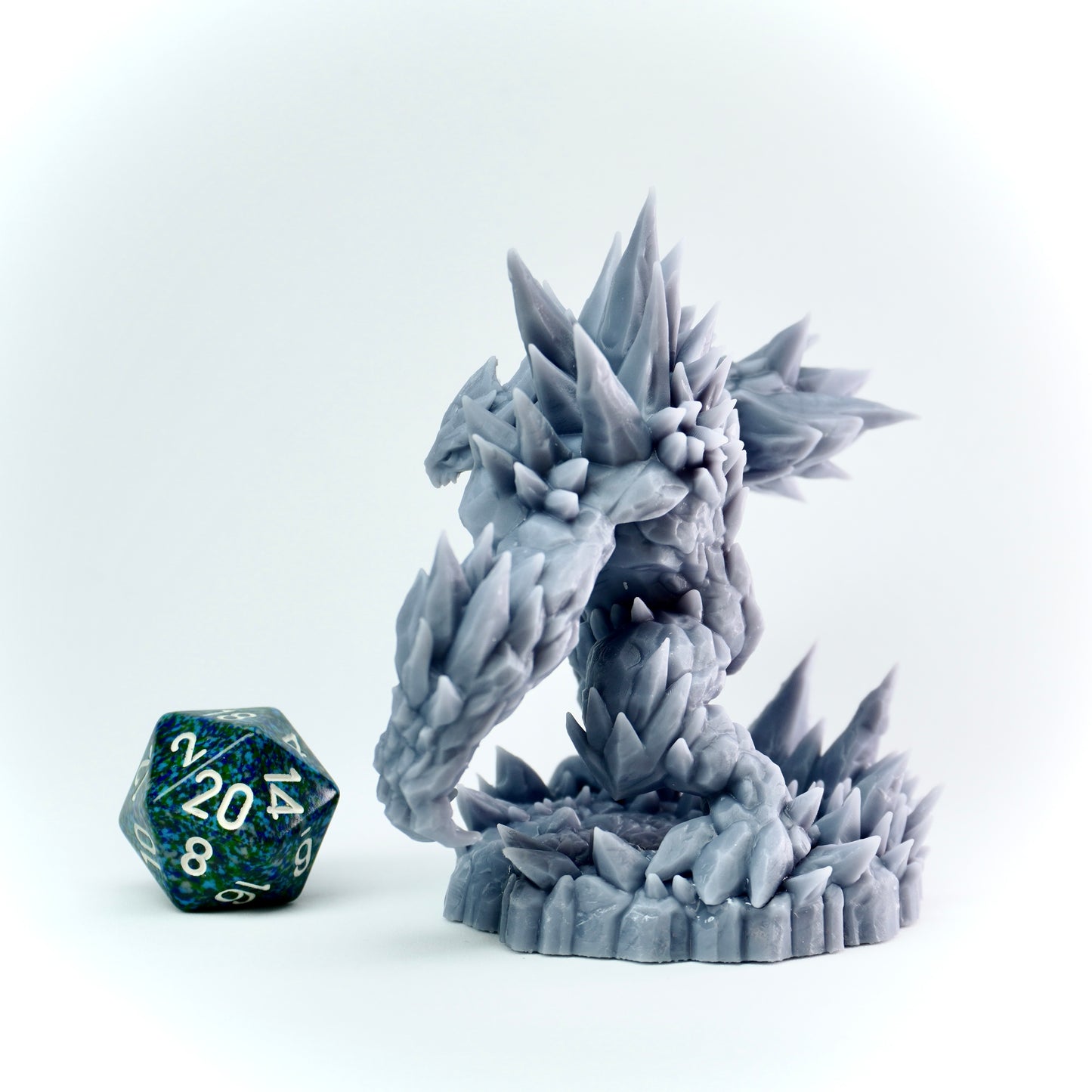 Gray spiked figurine with a blue and green polyhedral dice on a light gray background