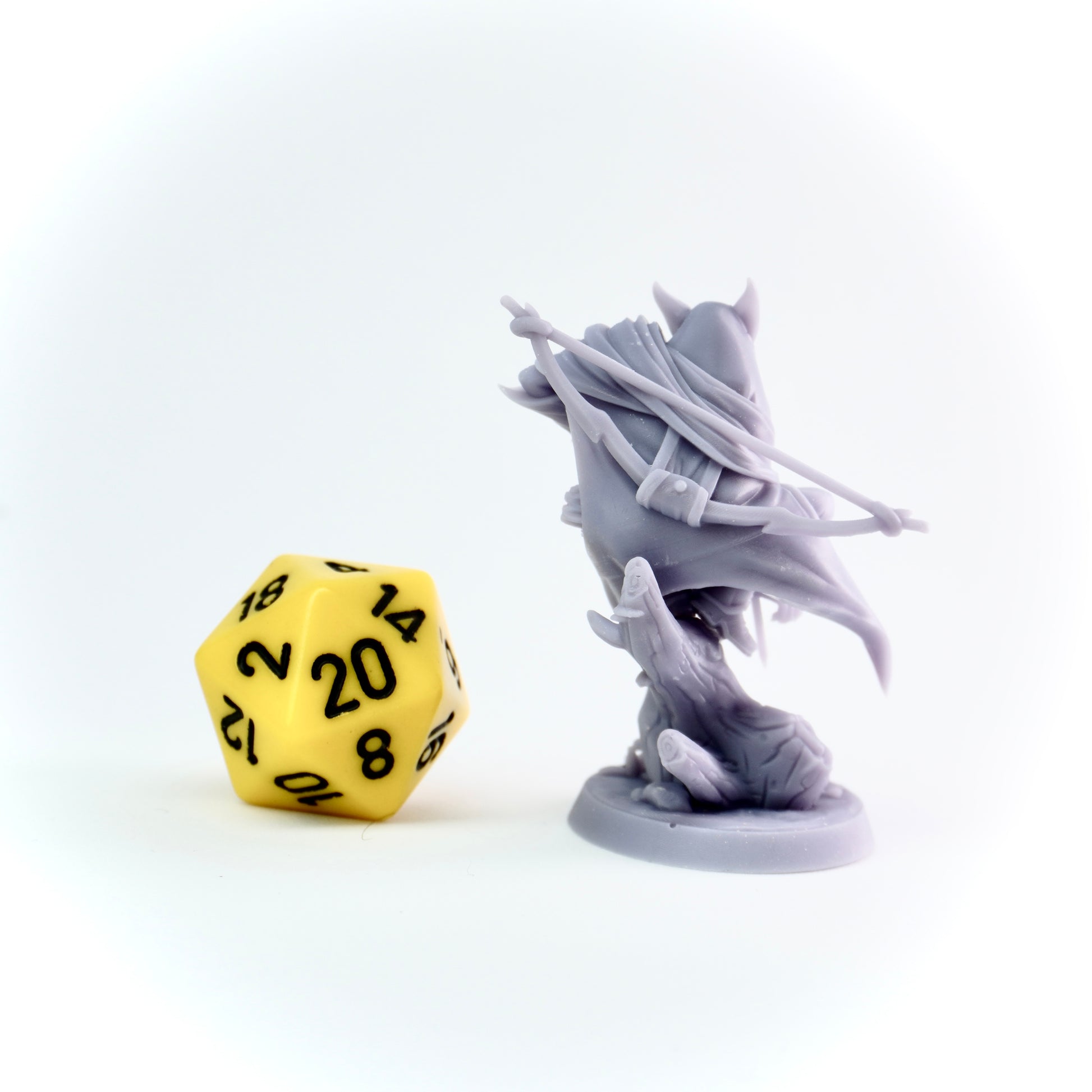 Gray fantasy figurine next to a yellow polyhedral dice on a white background