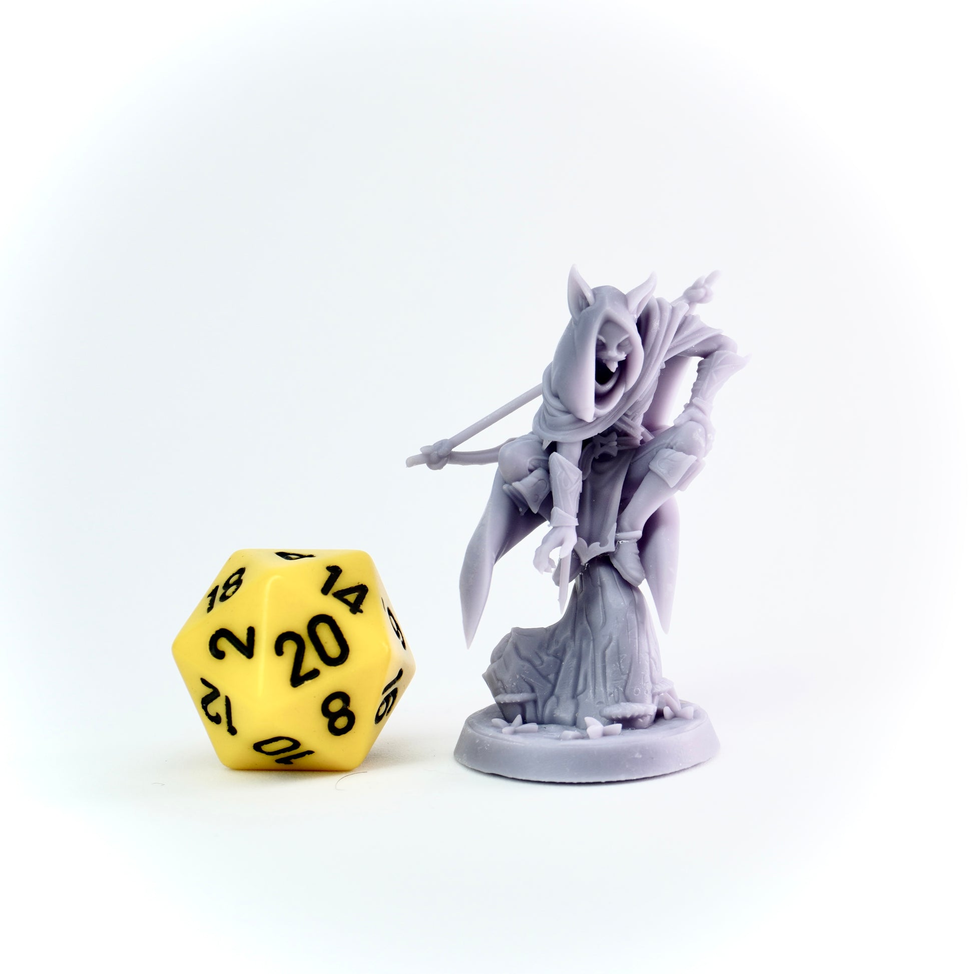 Gray fantasy figurine next to a yellow polyhedral dice on a white background