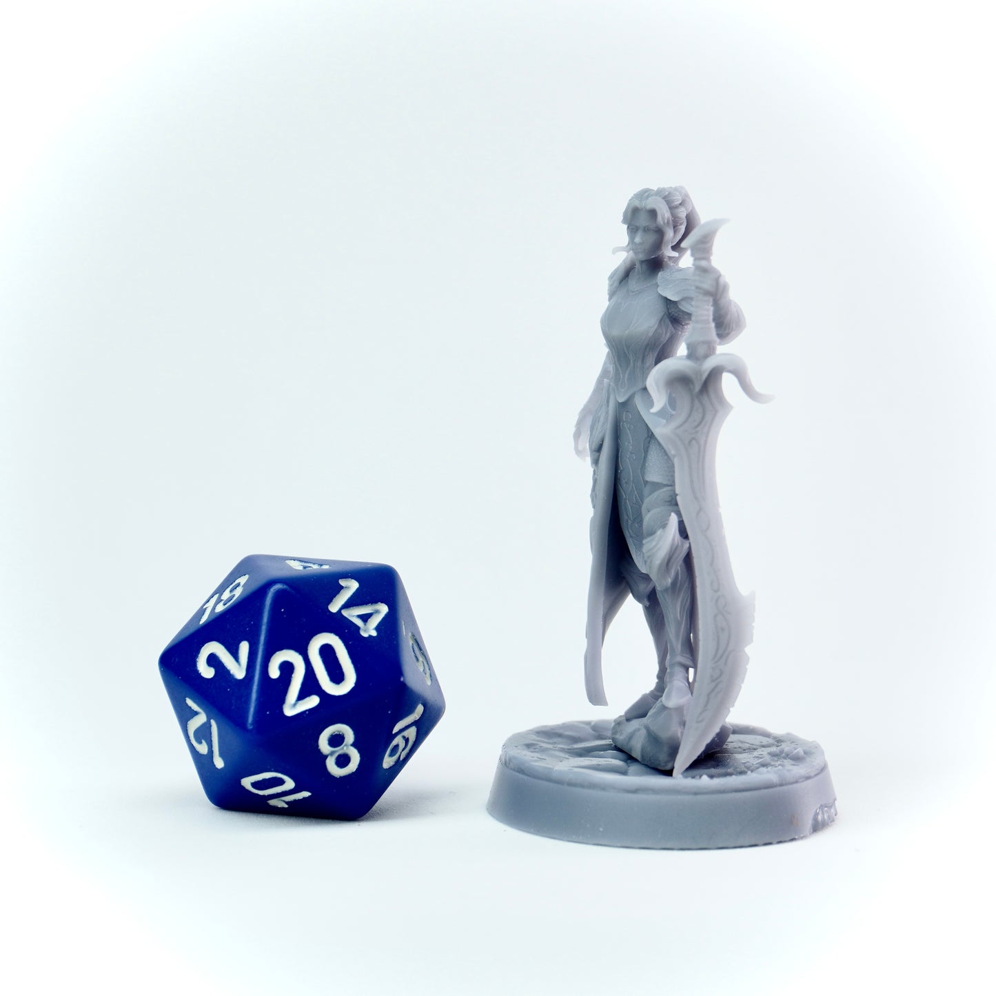 Gray fantasy figurine next to a blue polyhedral dice on a white background