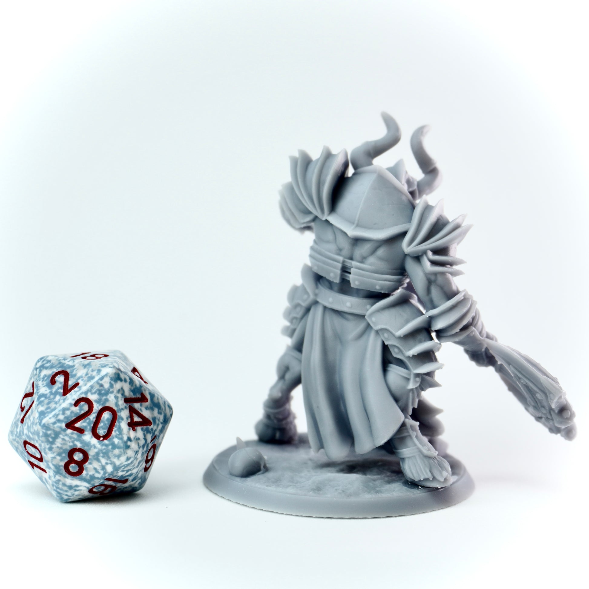 Gray fantasy figurine with armor and a weapon next to a polyhedral dice on a white background