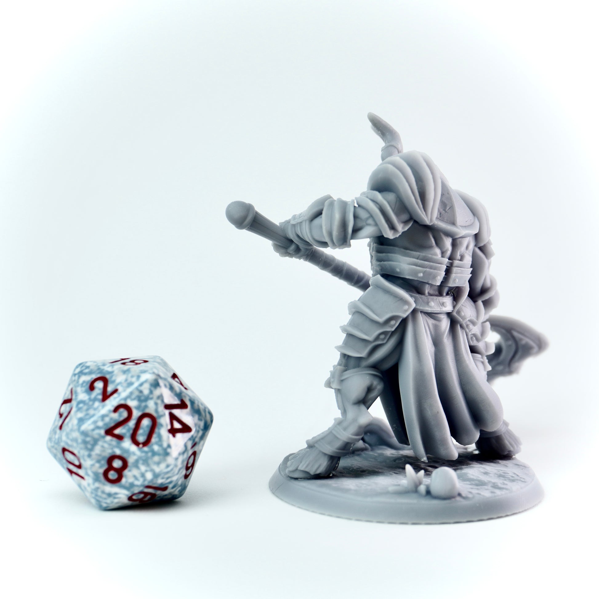 Gray miniature figure of a warrior with a weapon, next to a 20-sided die on a white background