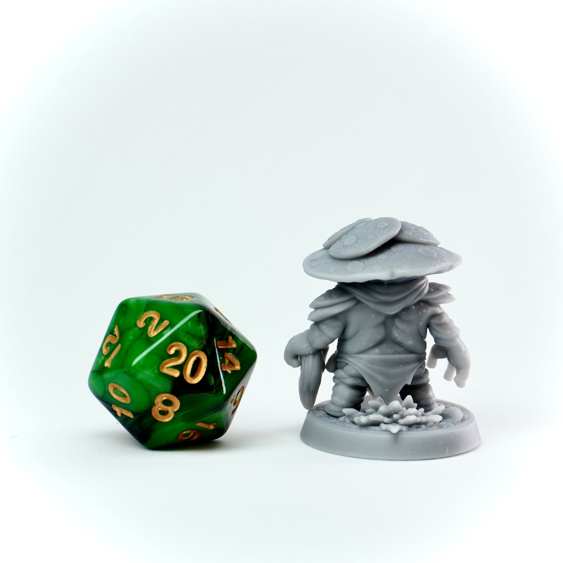 Gray miniature figure of a character with a mushroom hat next to a green polyhedral dice on a white background