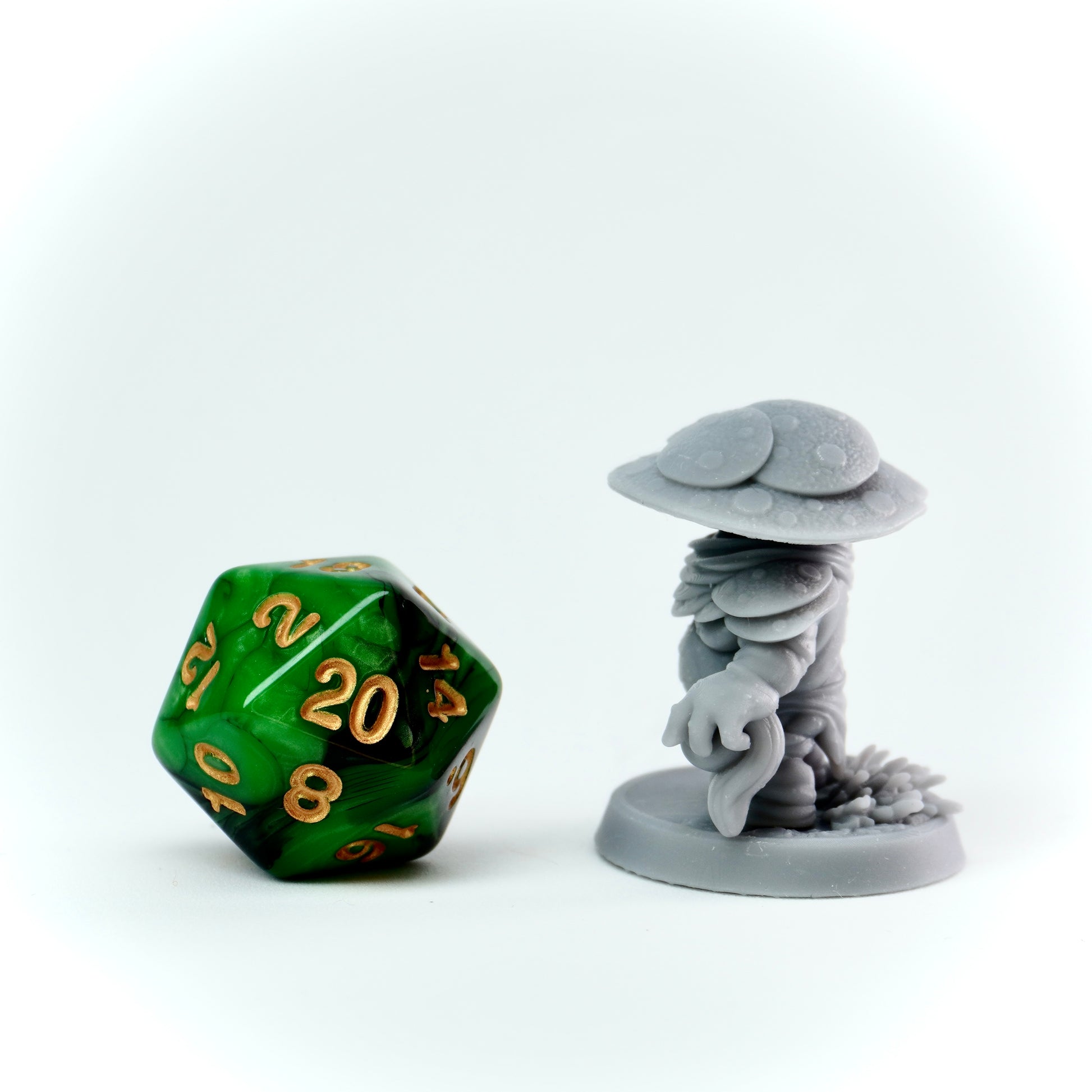 Green polyhedral dice next to a gray mushroom-like figurine on a white background