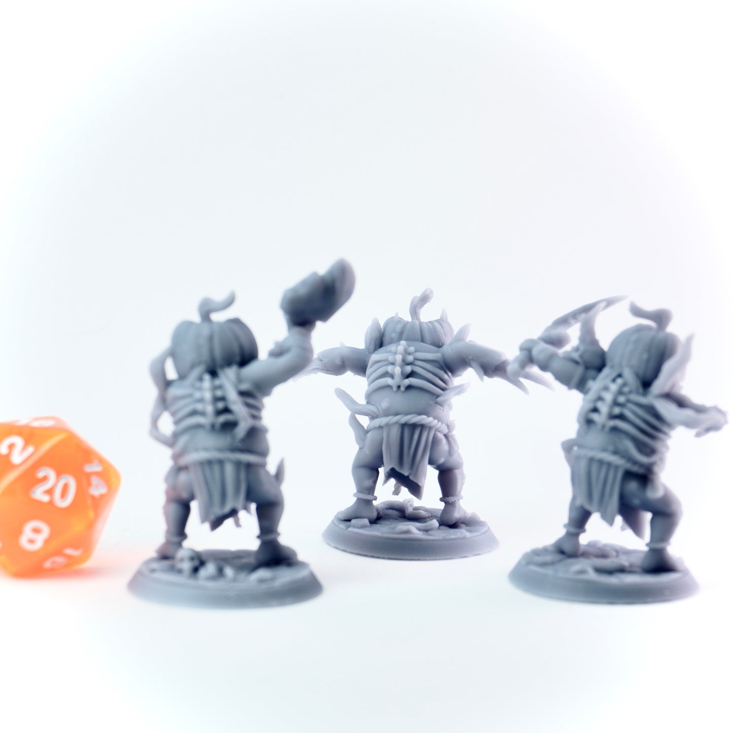 Three gray miniature pumpkin minion figures with a 20-sided die on a white background