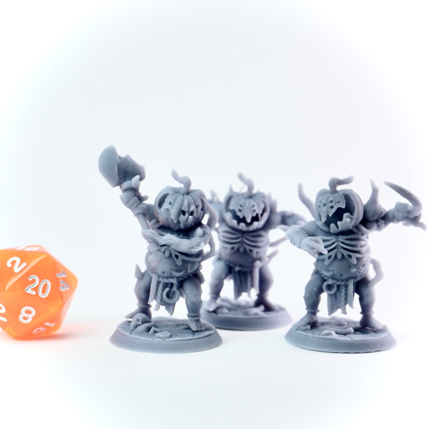 Three gray pumpkin minions miniature figures of skeletons with a orange dice on a white background
