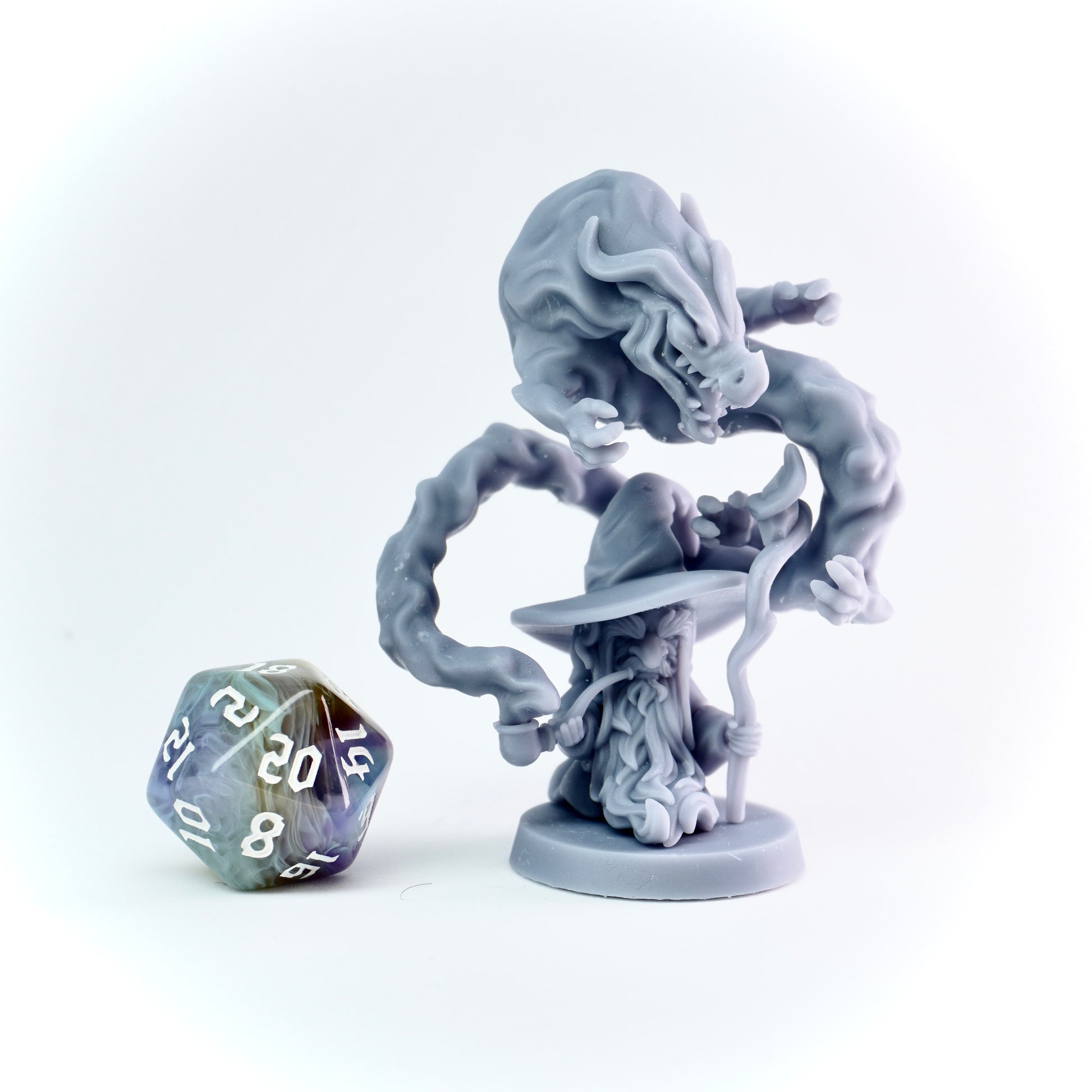 Gray fantasy figurine of a wizard being attacked by a smoke dragon with a polyhedral dice on a white background