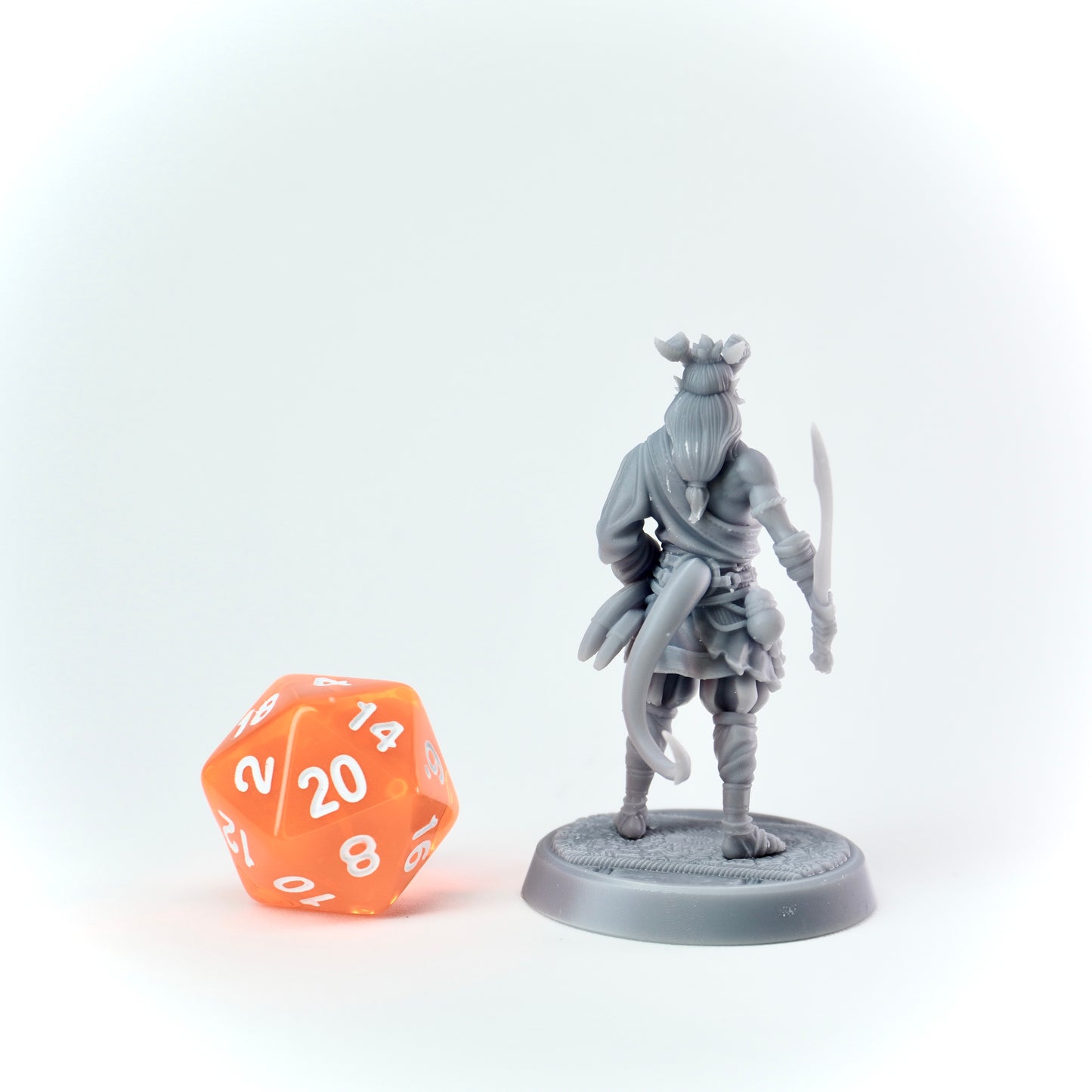 Gray miniature figurine of a warrior with a sword next to an orange polyhedral dice on a white background