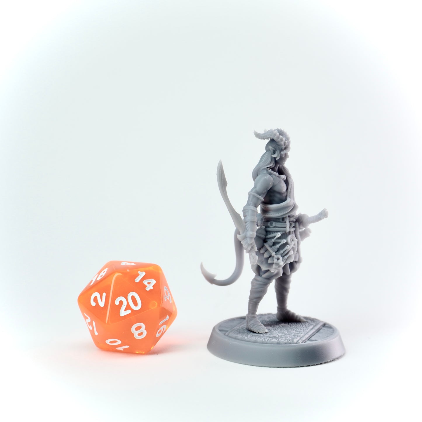 Gray fantasy figurine next to an orange polyhedral dice on a white background