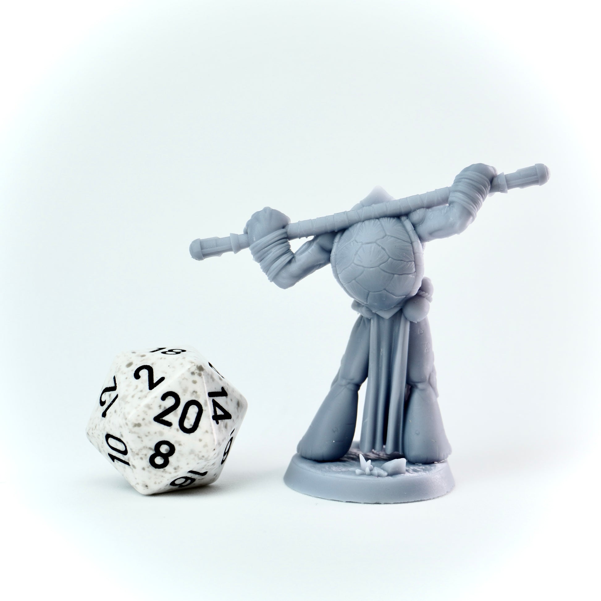 Gray miniature figure with a staff next to a twenty-sided die on a white background