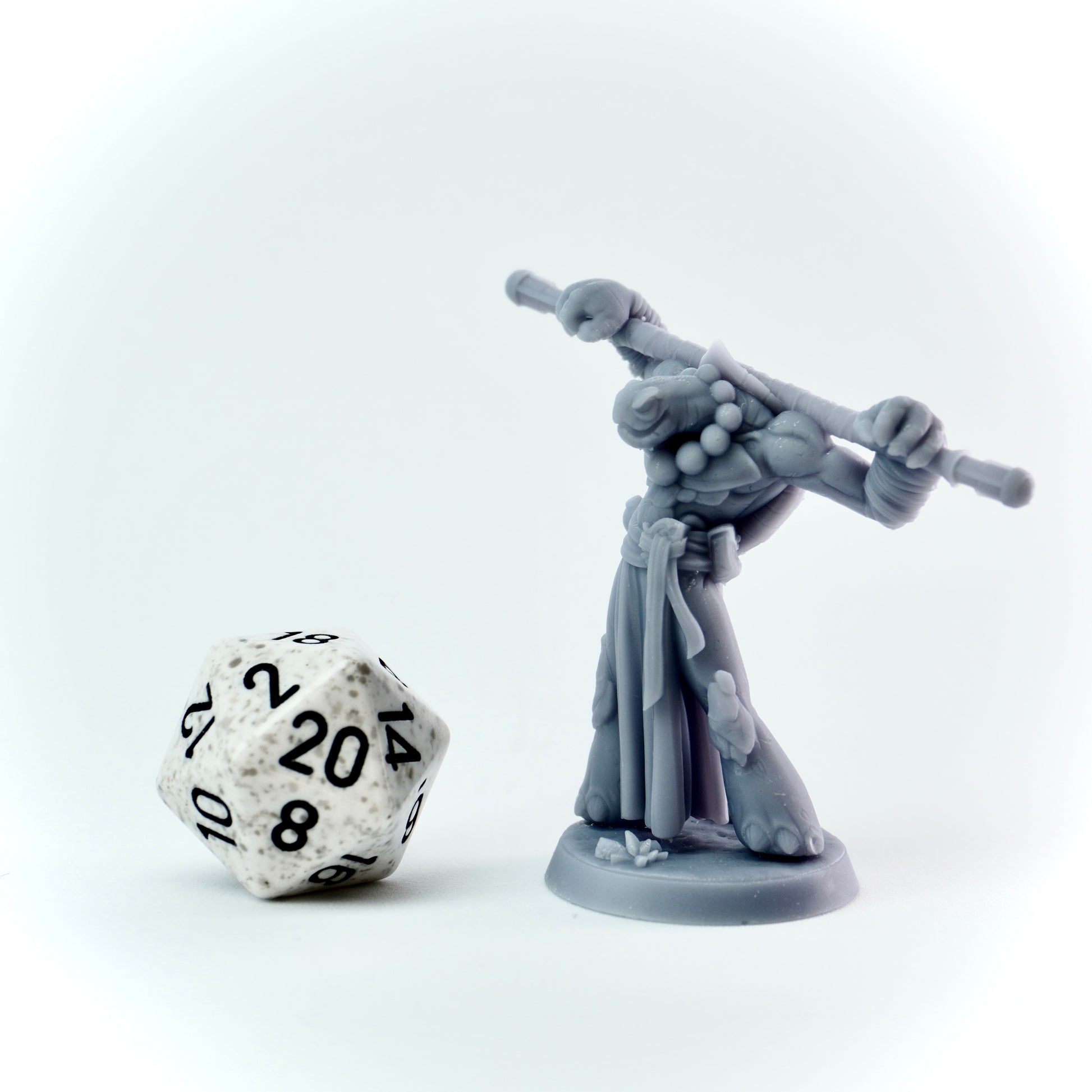 Gray miniature figure with a staff next to a twenty-sided die on a white background