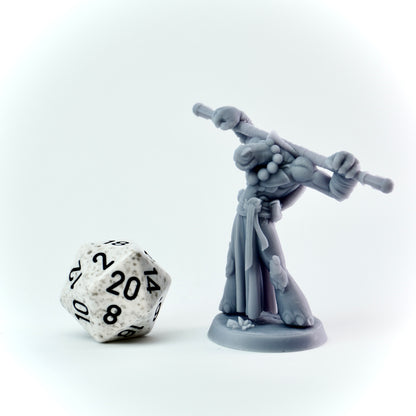 Gray miniature figure with a staff next to a twenty-sided die on a white background