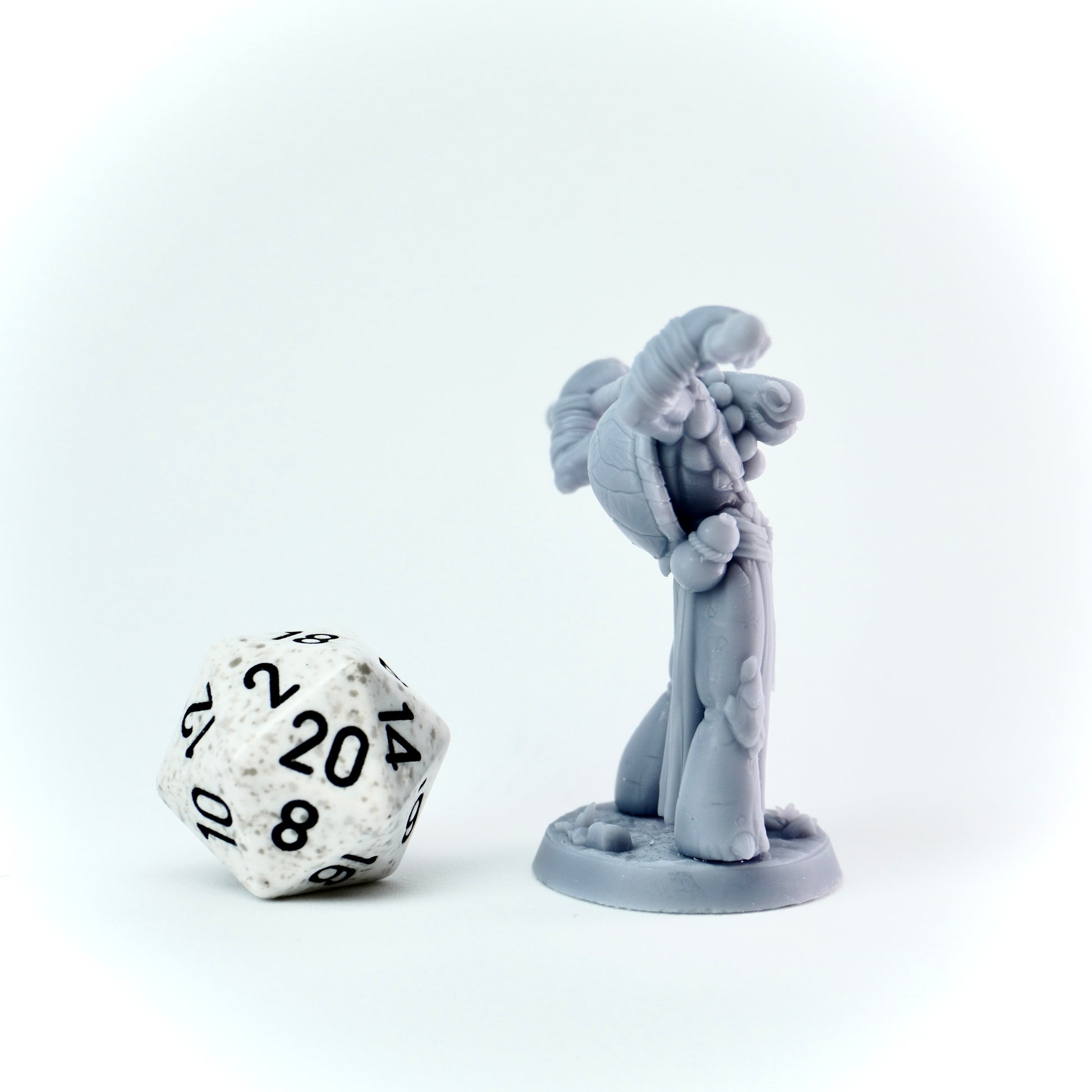 Gray miniature figure with a staff next to a twenty-sided die on a white background