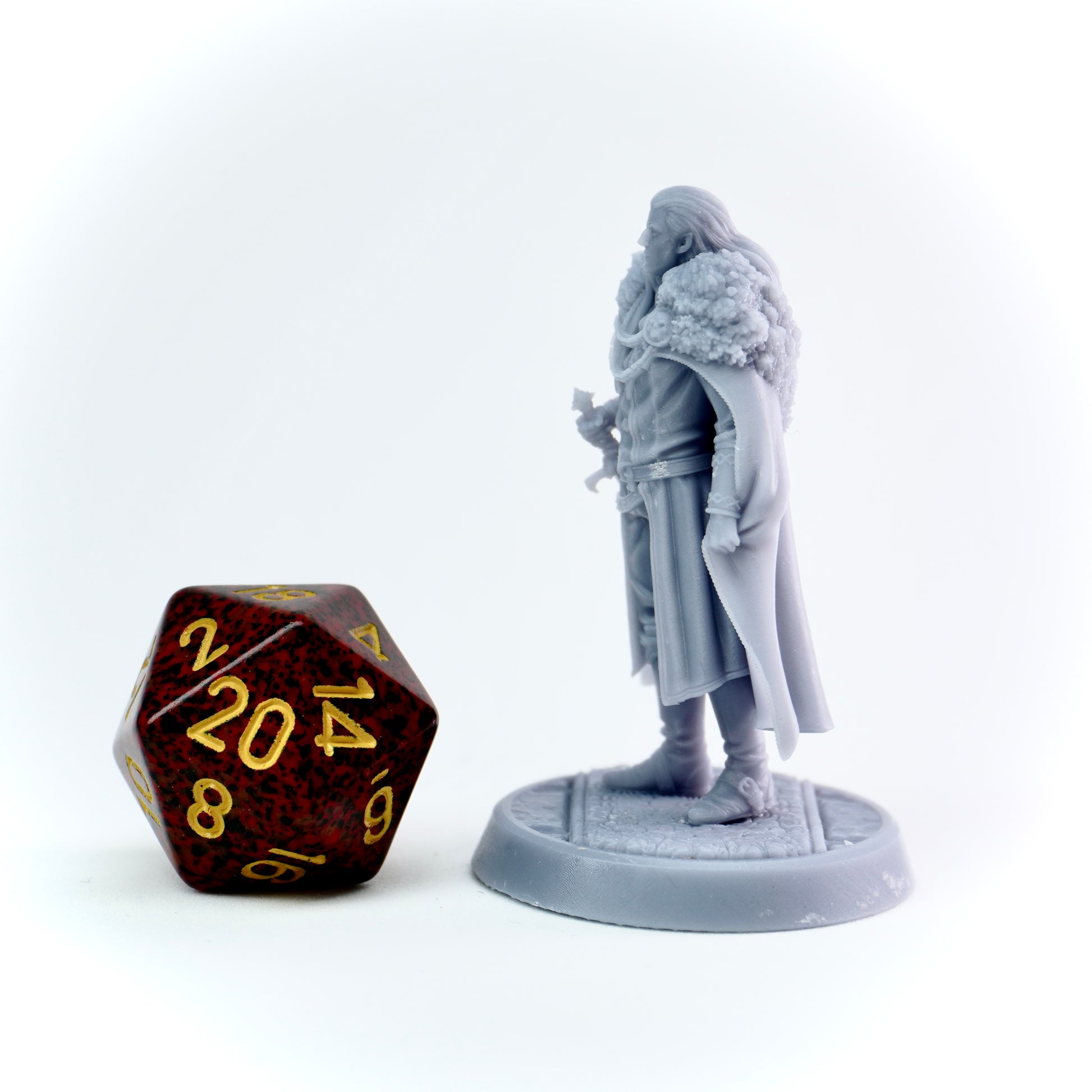 Miniature figurine of a character in a gray cloak next to a D20 dice on a white background