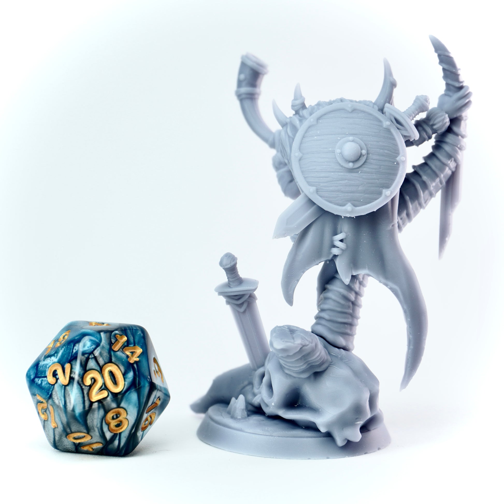 Gray fantasy figurine with a sword and shield next to a blue and gold polyhedral dice on a white background