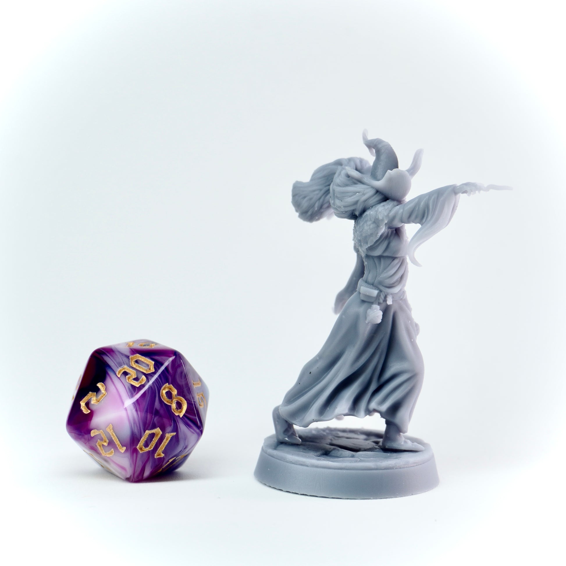Gray fantasy figurine next to a purple and gold polyhedral dice on a white background