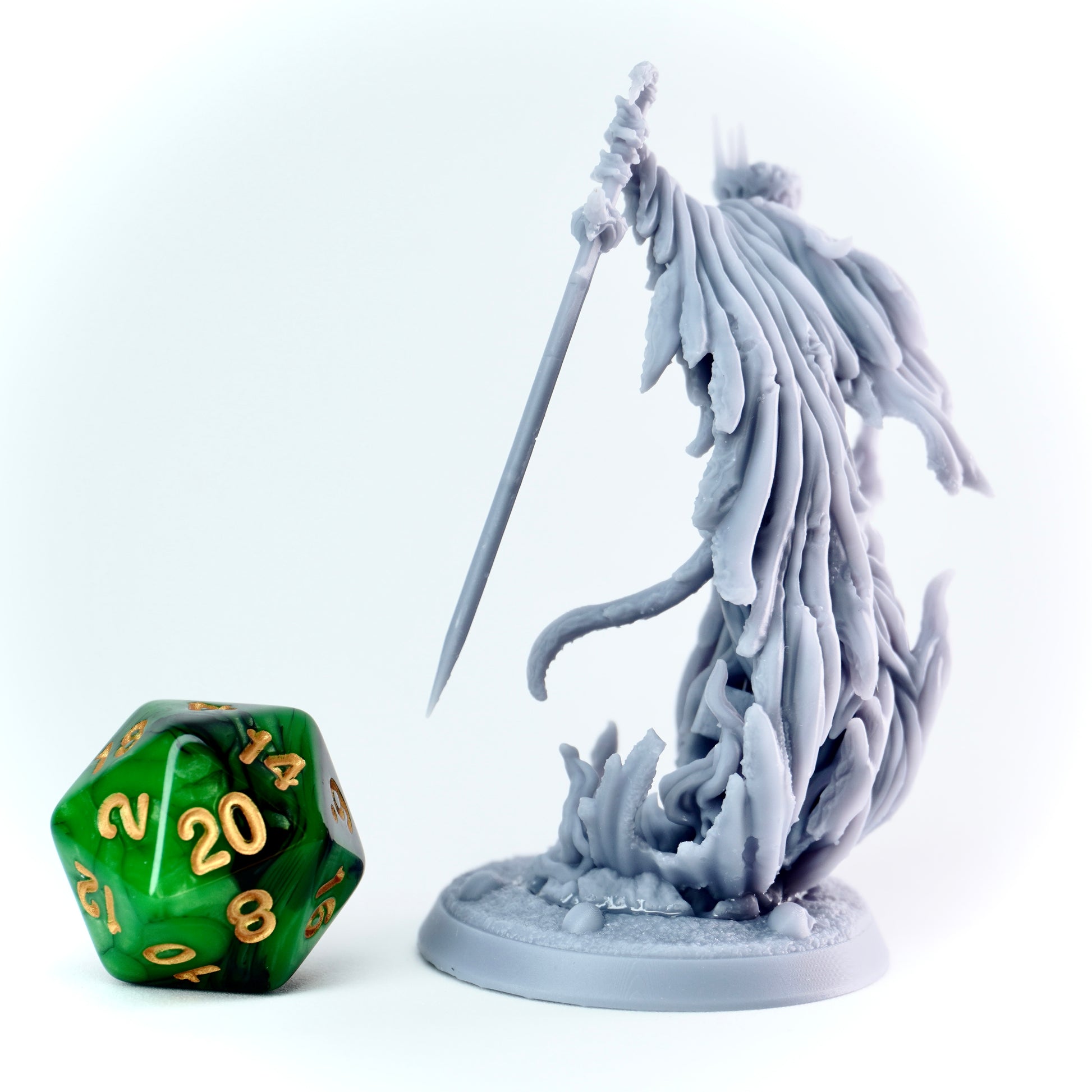 Gray fantasy figurine with a longsword next to a green polyhedral dice on a white background